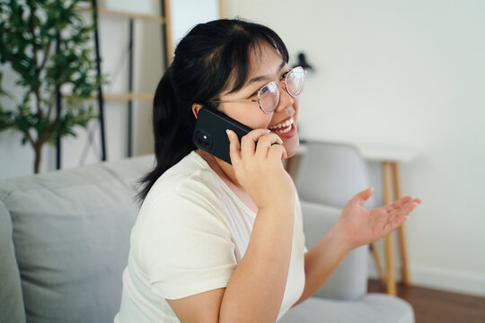 Asian woman holding smartphone to her ear, smiling while having a fun conversation