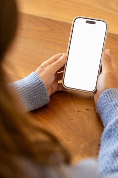 Person is holding a modern smartphone with a white empty screen over a wooden surface, showing communication, technology, and digital lifestyle concepts with ample space for custom content