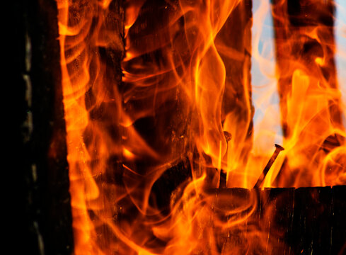 Bright orange fire flames burning between charred wooden logs background texture