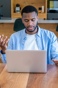Man feeling frustrated while gesturing with his hands during a video call or online meeting, experiencing communication difficulties or technical problems while working from a home office
