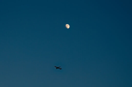 Minimalist scene of airplane and moon in deep blue twilight sky