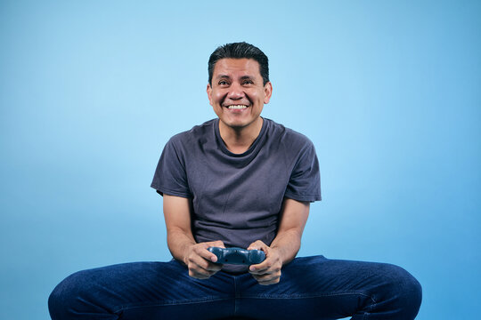 adult Latin man gamer playing video games and holding game controller with copy space on blue background in Mexico Latin America