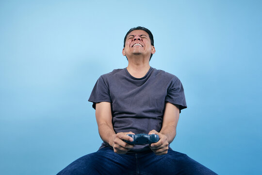 adult Latin man gamer playing video games and holding game controller with copy space on blue background in Mexico Latin America