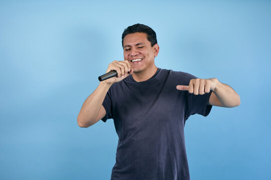 portrait of adult latin man holding a microphone and singing in karaoke on blue background in Mexico Latin America