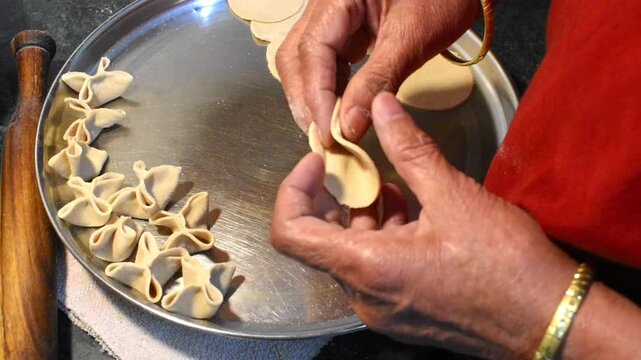 elderly woman's hands shaping small dough pieces into traditional dal pitti by hand in a home kitchen. food preparation process showing Indian cuisine and traditional cooking techniques