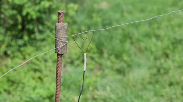 Close-up of electric fence wire wrapped around a rusty metal post in a grassy outdoor area. Rural agricultural detail showing livestock fencing equipment and countryside infrastructure