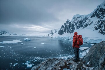 Fototapeta premium Hiker in bright orange jacket looking at icy glacial landscape in antarctica with antarctica mountain expedition adventure landscape wilderness climbing trekking backpack environment