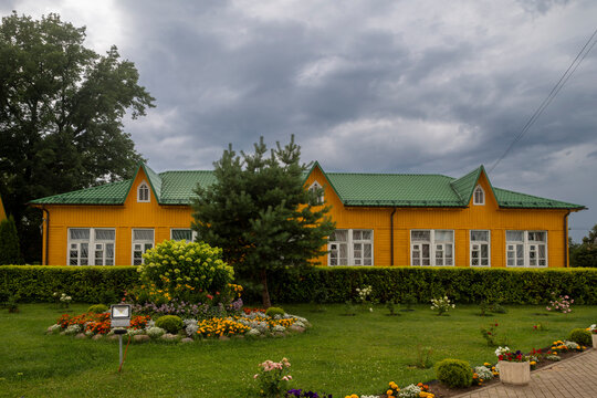 Kimry, Tver Oblast, Russia, July 25, 2026 - Yellow wooden building with green roof and garden flowerbeds under stormy sky. The Sunday School building at the Church of the Ascension