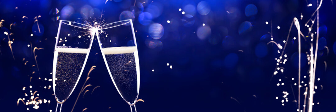 two clinking champagne glasses isolated on dark blue background with abstract fireworks, greeting card with copy space for new year party and december holiday season