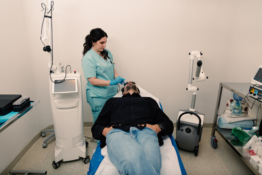 Derm in blue scrubs preps patient for skin procedure in clinic room.
