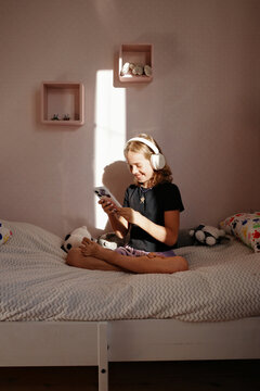 Teen sitting on bed using smartphone with headphones