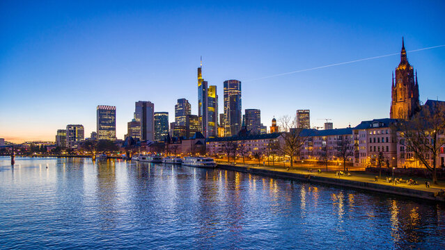 Frankfurt, Germany, a view of the illuminated financial district from the Main river with sightseeing boats at blue hour and cloudless sky  in the evening