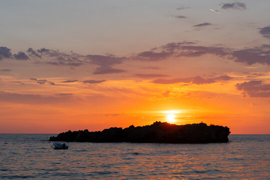 A small boat drifts beside a rocky islet at sunset