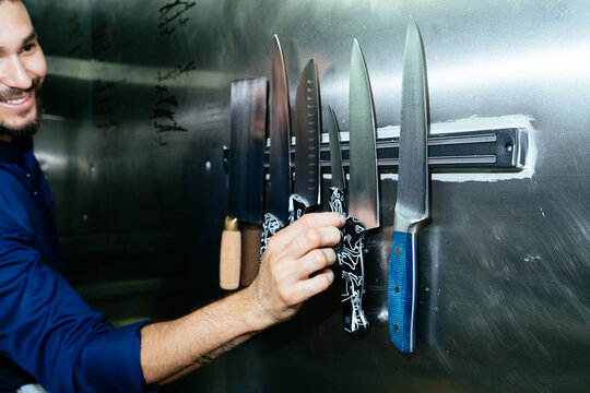 Chef organizing professional kitchen knives on magnetic strip