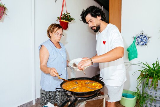 Young man and older woman cooking paella outdoors
