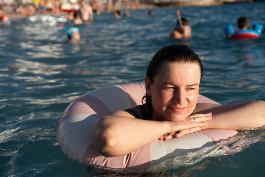 A woman floats on a pink ring in a busy summer sea