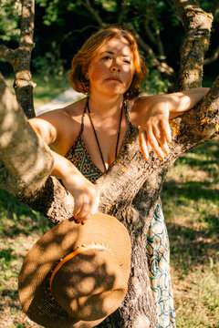 Woman Resting on a Tree While Holding a Hat in a Sunny Spot