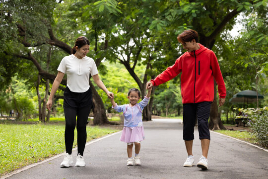 Parents are here reate perfect day for childrent. Father and mother hands and raise her up and walk. exercising and walking together in city park summer. healthy lifestyle in nature. family bonding