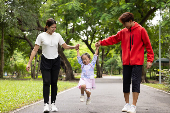 Parents are here reate perfect day for childrent. Father and mother hands and raise her up and walk. exercising and walking together in city park summer. healthy lifestyle in nature. family bonding