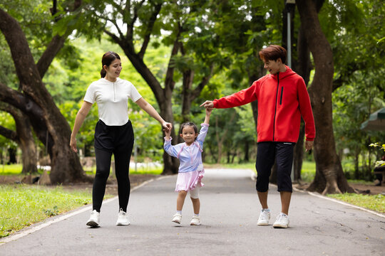 Parents are here reate perfect day for childrent. Father and mother hands and raise her up and walk. exercising and walking together in city park summer. healthy lifestyle in nature. family bonding