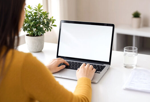 Young woman working on a laptop at a clean desk with plant and water glass beside her