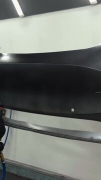Professional auto body painter applying primer to a car bumper with spray gun