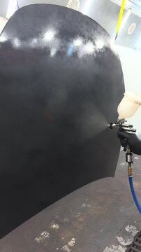 Professional auto body painter applying black primer with spray gun in booth