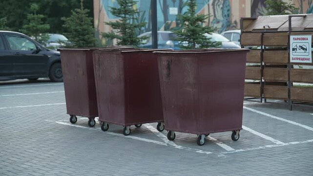 Three brown metal dumpsters on wheels standing in a parking lot