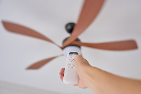Hand using remote control to adjust ceiling fan speed in residential interior