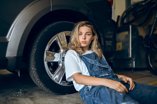 Girl sitting on ground near car in a garage while looking at camera in the afternoon