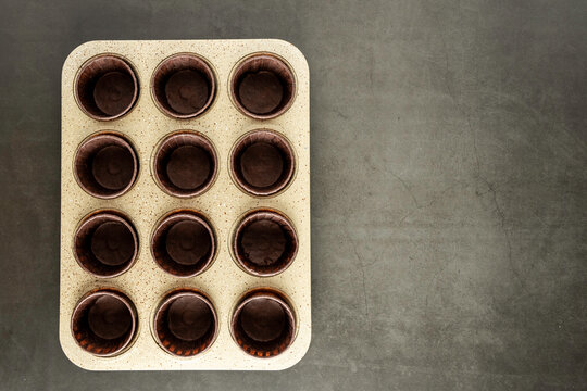 Muffin pan with brown paper liners on a dark surface 