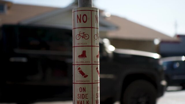 A sign on a post in California states no bikes, no skateboards, and no rollerblades are allowed on the sidewalk.