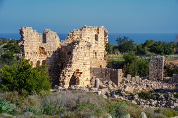 Fototapeta premium Ancient stone ruins overlook the Mediterranean Sea. Crumbling walls and amid green shrubs. Ideal for travel, archaeology, history, and cultural heritage editorial use.