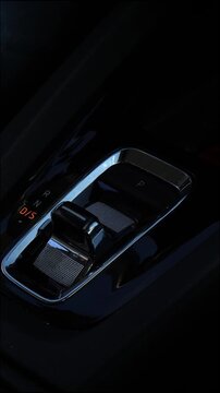 Female hand with neat manicure switching automatic transmission gear shift lever inside luxury car cabin.
