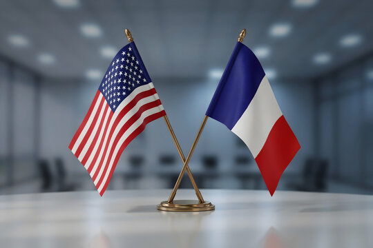Small desk flags of the united states and france standing on a white table inside a blurred conference room for diplomatic meetings
