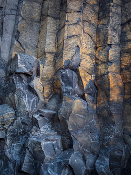 Hexagonal basalt columns and volcanic rock formations rise from black sand at Reynisfjara beach near Vik, Iceland.