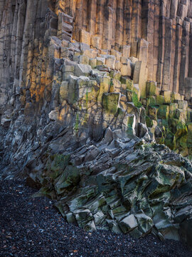 Hexagonal basalt columns and volcanic rock formations rise from black sand at Reynisfjara beach near Vik, Iceland.