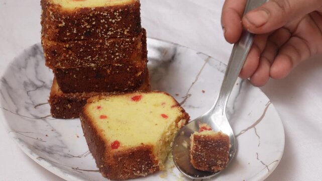 Woman's hand eating a slice of fruitcake, cutting and serving it with a stainless-steel spoon. Delicious dessert fruit cake meal food snack on a white plate.
