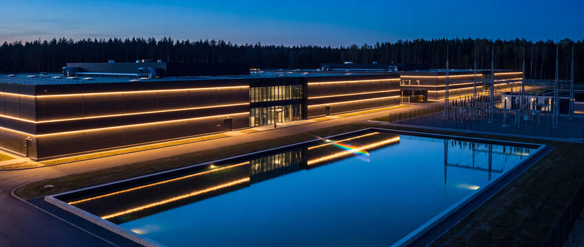 Data center building illuminated at night features dark sleek architectural panels, warm LED exterior lights, and a clear water reflection for modern cloud computing technology