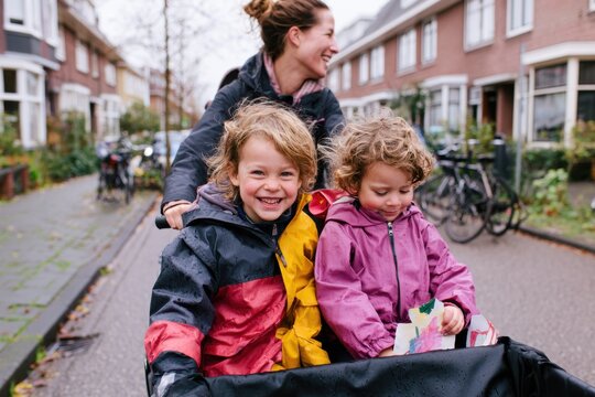 happy woman riding a cargo bike with two smiling children in a dutch neighborhood