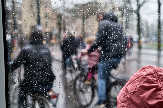 rainy day street scene with people on bicycles viewed through a wet window