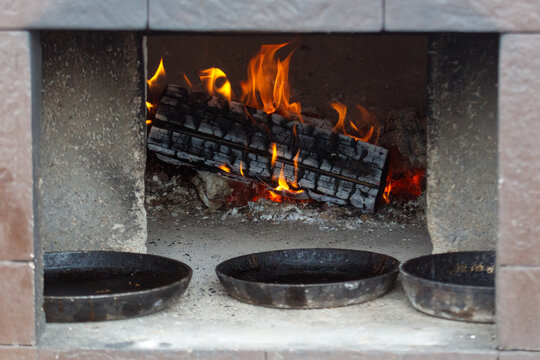 Fire burns inside stone oven with three cast iron pans below.