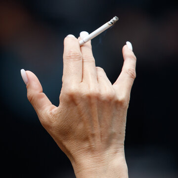 Hand holds cigarette against dark blurred background