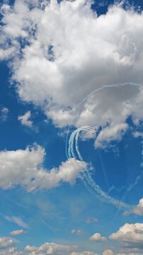 Aerobatic stunt aircrafts performing spectacular aerial maneuvers in the sky, releasing colorful smoke and fireworks. Team formation flight with white smoke trails. 4K vertical video footage