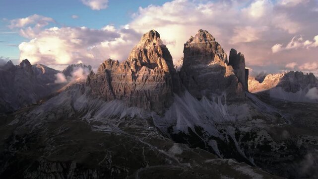 Cinematic aerial view flying toward the iconic Tre Cime di Lavaredo mountain peaks in the Italian Dolomites at sunset