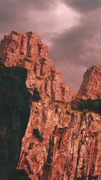 Tall rock formations stand against a backdrop of dark clouds. The landscape shows rugged terrain and steep cliffs. Nature surrounds this area, creating a dramatic view of the scenery.