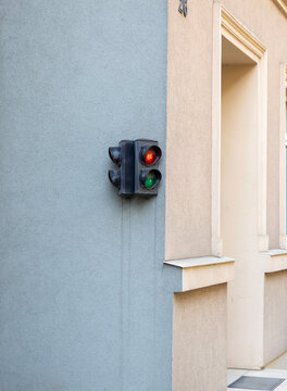 Small traffic signal mounted on beige stucco wall beside building entrance with red and green lenses, soft daylight, textured facade, recessed doorway, and calm urban architectural detail