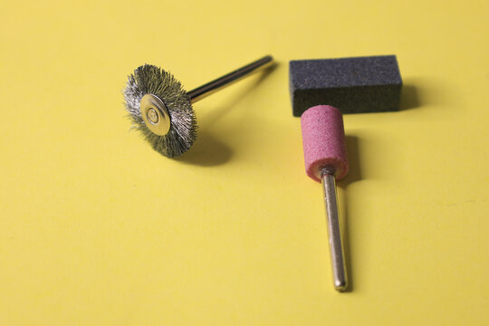 Rotary tool accessories on a yellow background &mdash; a wire brush, a pink grinding stone, and a rectangular abrasive block
