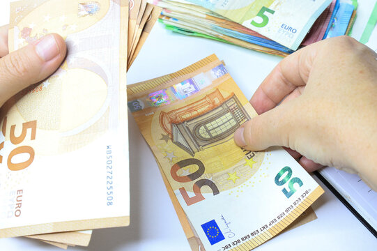 Two hands counting &euro;50 and &euro;5 euro bills with a stack of mixed denominations in the background &mdash; symbolizing cash handling, budgeting, or personal finance management