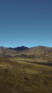 A broad landscape shows vast grasslands surrounded by steep mountains. The sun shines brightly in a clear blue sky. This scene presents a quiet moment in natures setting.